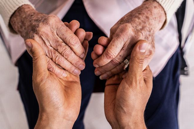 Một người chăm sóc đang nắm tay động viên người già bị mắc bệnh Alzheimer