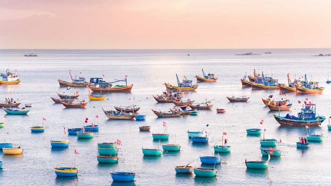 Một làng chài nhỏ ven biển với những ngôi nhà mái tranh ấm cúng, thuyền bè neo đậu trên bờ cát dưới bầu trời xanh