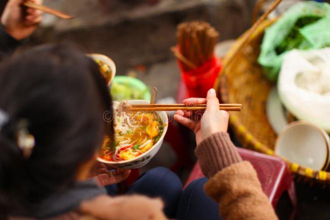 Một nhóm bạn trẻ đang thảo luận và chụp ảnh món ăn tại một quán ăn đường phố Việt Nam